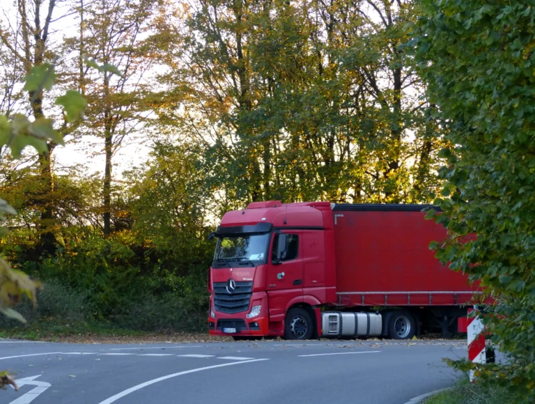 A large, red lorry turning the corner of a road lined with trees.