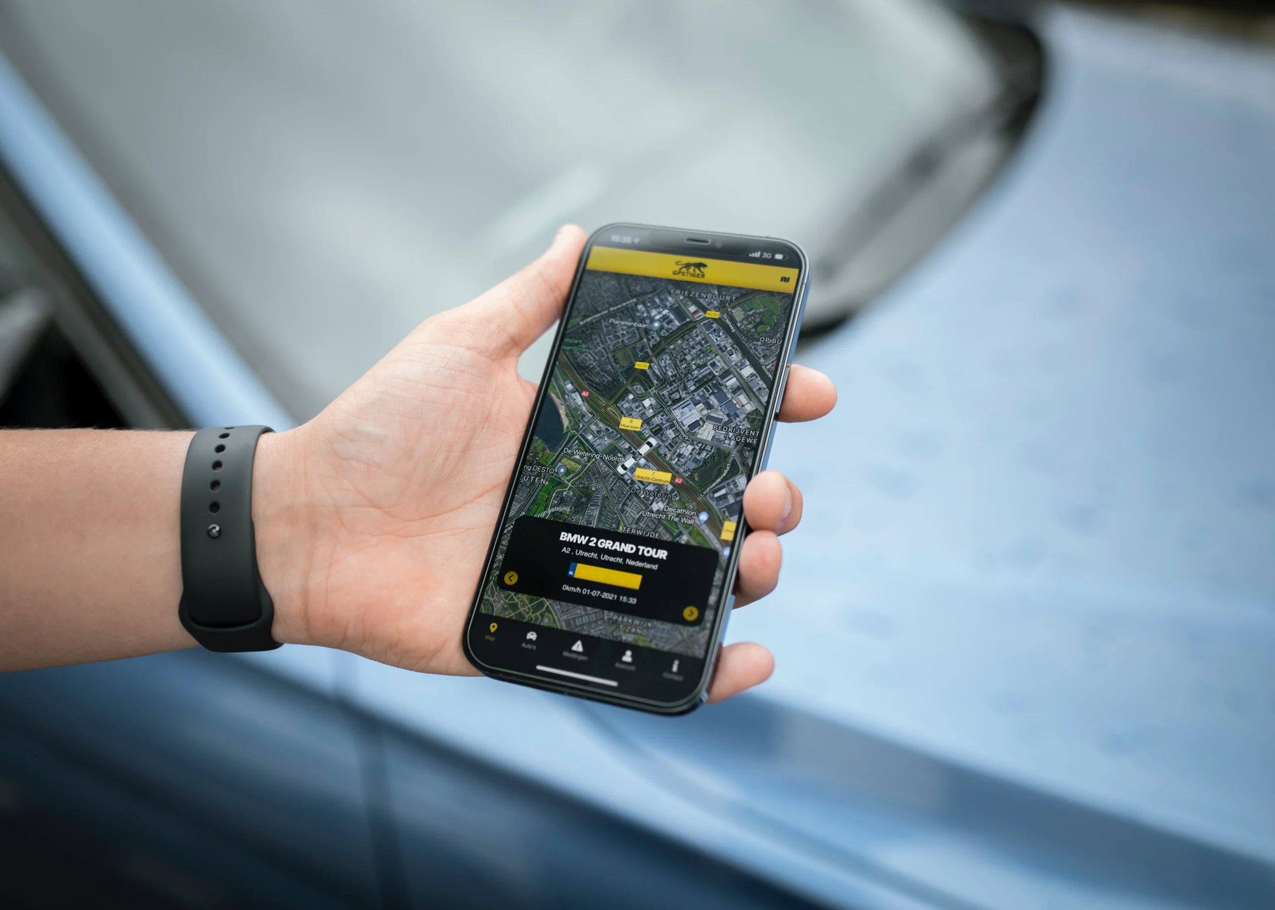 A person holding a mobile phone showing a vehicle tracking system in use